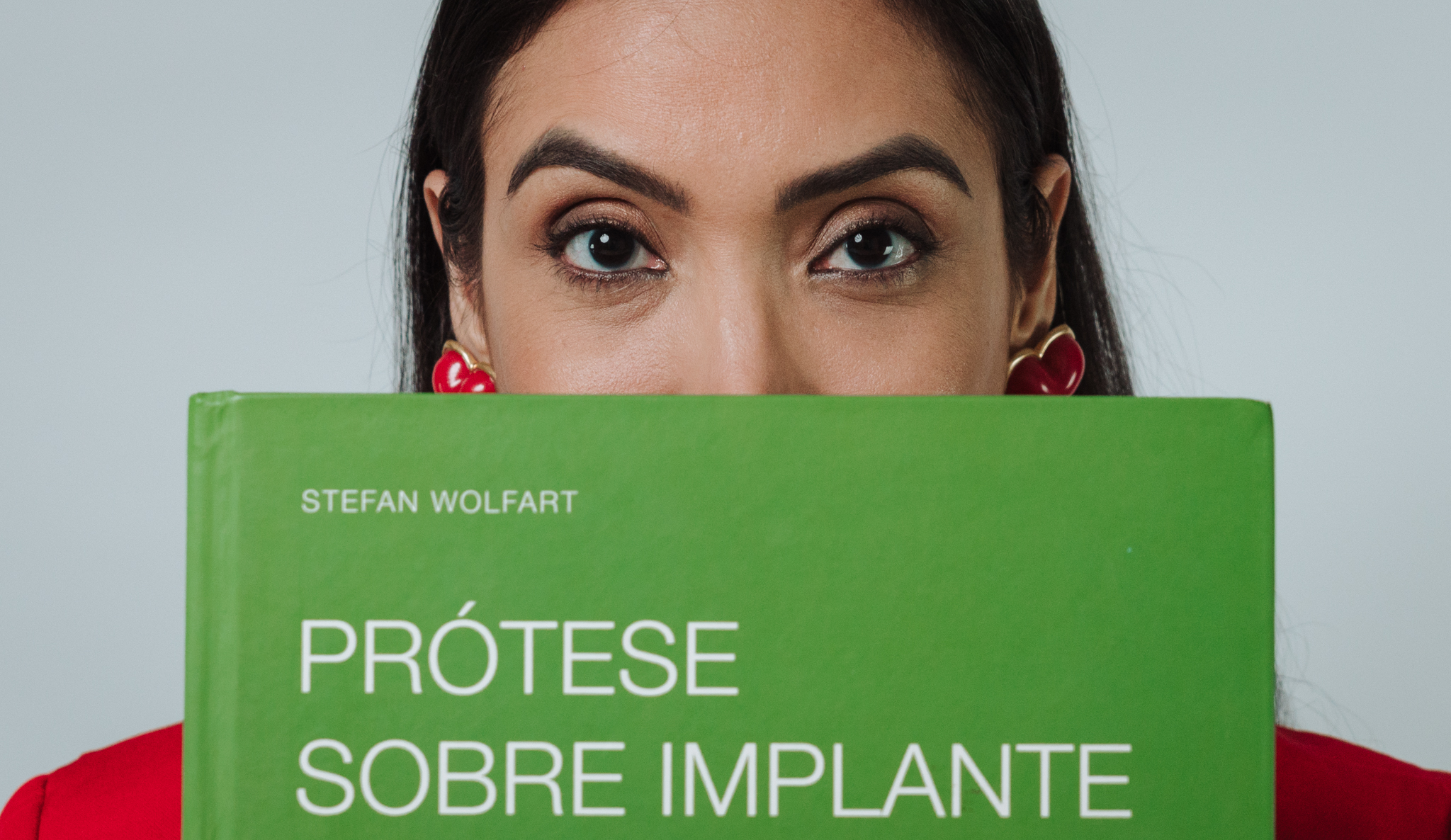 Dra. Catarina Silveira com o olhar em destaque atrás do livro Prótese sobre Implante, de Stefan Wolfart