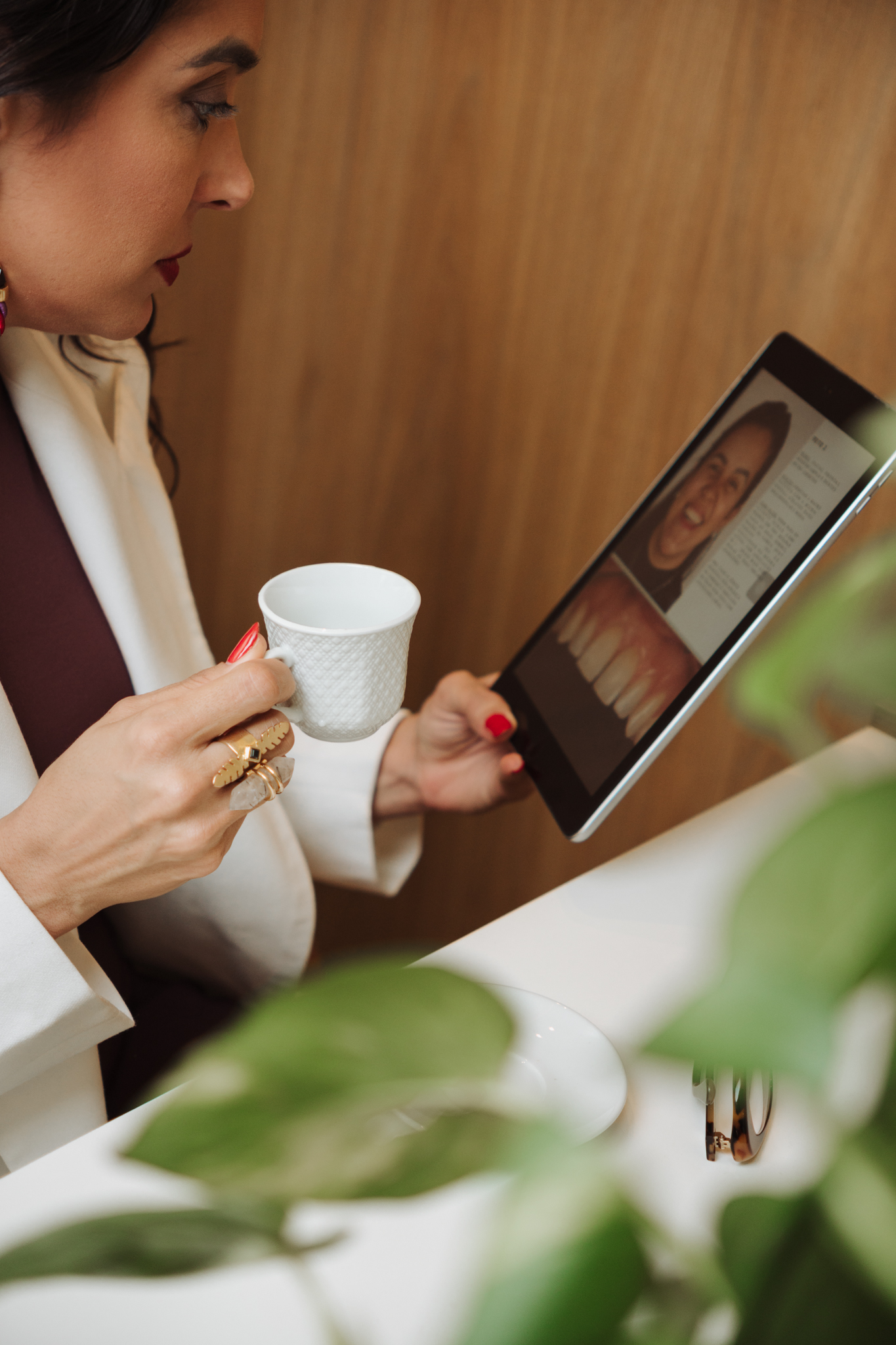 Dra. Catarina Silveira analisando registros clínicos de um caso em um tablet, com uma xícara de café na mão