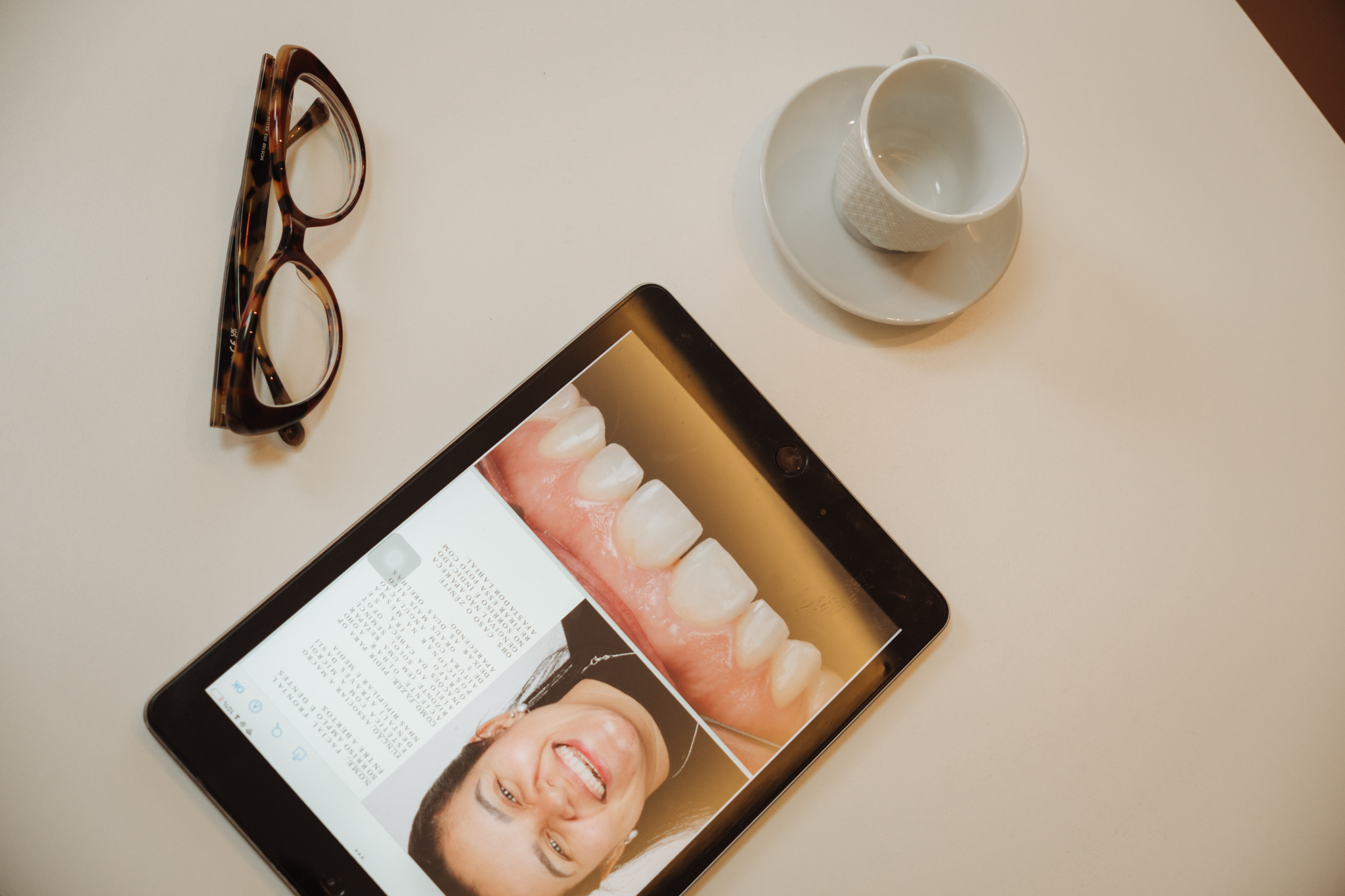 Tablet sobre a mesa exibindo fotografias clínicas de um caso de reabilitação, ao lado de óculos e xícara de café